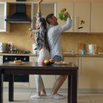Attractive young joyful couple have fun dancing and singing while cooking in the kitchen at home in the morining